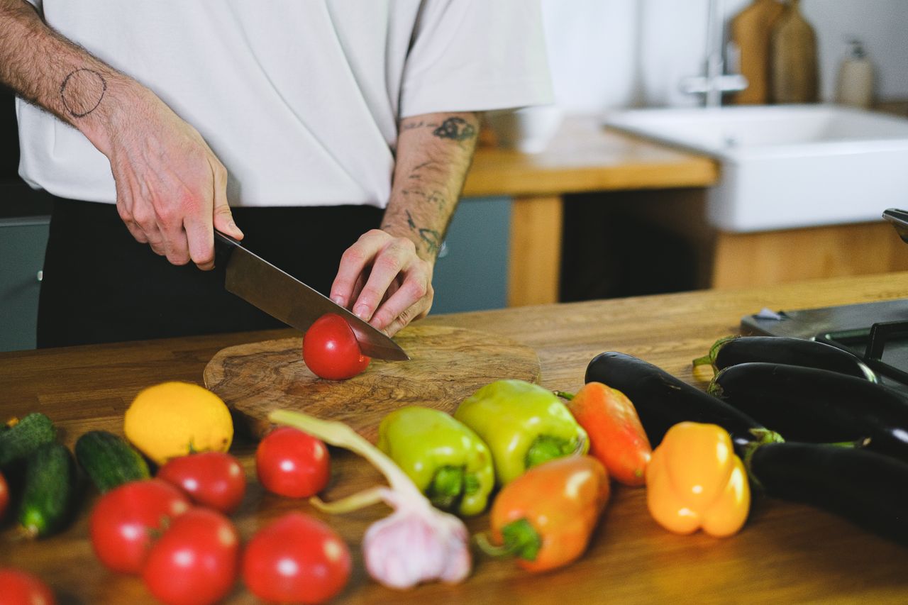 services-02 A person slicing tomatoes on a wooden board among fresh vegetables in a kitchen setting.
