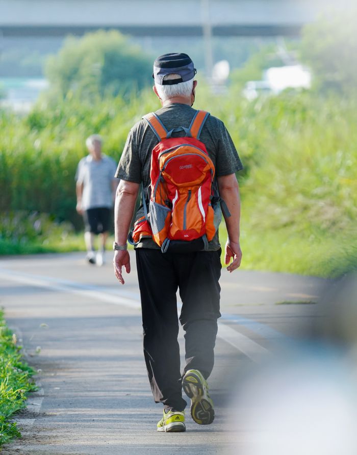 our-experience Senior man with backpack walking on a sunny urban trail, showcasing outdoor lifestyle.