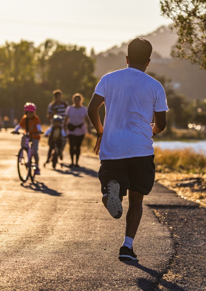 services-04 Man jogging along a scenic path at sunset with cyclists in the distance.