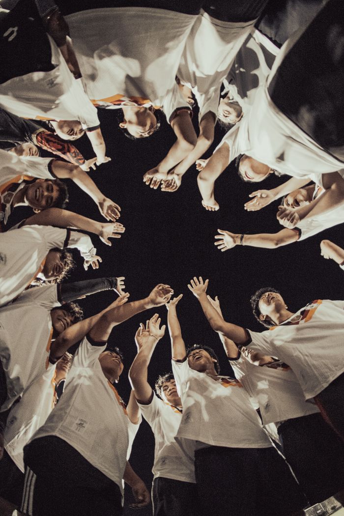 contact-img A group of people forming a circle and reaching out towards the night sky, symbolizing unity and teamwork.