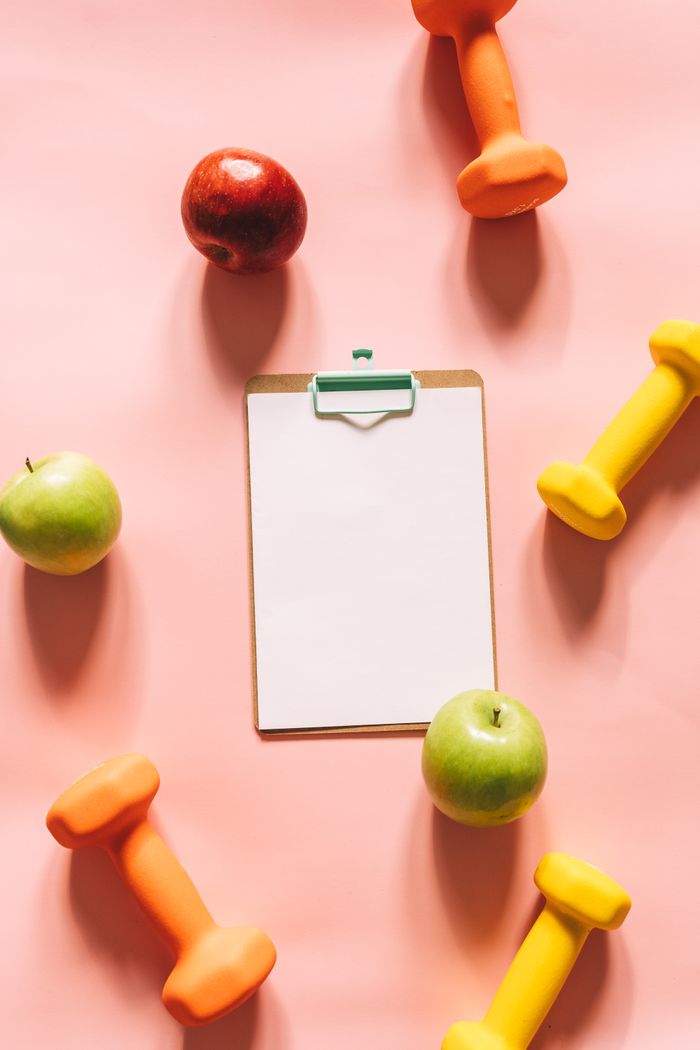 about-02 Top view of colorful apples, dumbbells, and clipboard on a pink background, ideal for health and fitness themes.